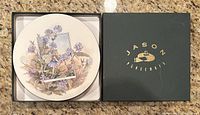 Set of six round placemats with floral fairy artwork stacked in original box, showing box top reading "JASON PLACEMATS" in gold on dark green