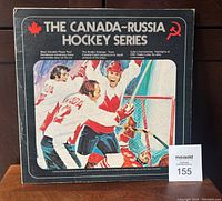 Front cover of The Canada-Russia Hockey Series LP showing illustrated ice hockey scene with Canadian players celebrating a goal near the net. Red maple leaf and Soviet hammer and sickle icons in title area.