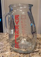Clear glass Evenflo pitcher showing front vertical red brand name and measurement markings in ounces and cups.
