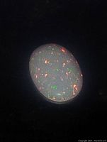 Close-up photo of oval cabochon Ethiopian fire opal showing multicolored fire speckle on a dark background.
