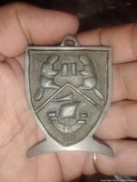 Front view of the pewter beaver display plaque held in hand, showing two beavers and sailing ship emblem in relief.