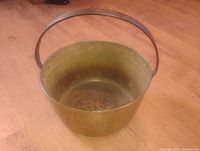 Solid brass antique Victorian jam pan shown from above on wooden floor, handle standing upright.