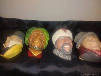 Four bosom head figurines arranged side by side on a black cloth background, showing overall collection and variety of styles.