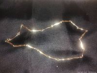 Gold plated chain necklace arranged on a black fabric background, highlighting the links and reflective shine.