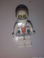 Single white Lego space man minifigure photographed upright on a flat surface with visible printed details on torso and face, wearing a helmet with yellow visor.