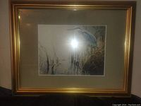 Framed print showing a blue heron among reeds with gold frame and beige matting.