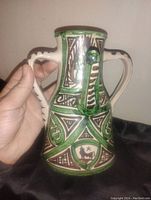 Front angled view showing the jug's spout, handle, and detailed painted geometric and animal designs in green, brown, and black.