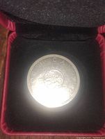 Close-up of the coin in the velvet-lined box showing front floral design and inscriptions.