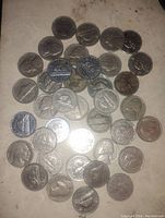 Top down photo showing a spread of older USA and Canadian 5 cent coins on a beige surface. Multiple coin types visible including Jefferson and Buffalo nickels, and Canadian nickels with beaver.