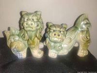 Front side view of both Asian foo dog pottery statues showing their faces, detailed curls, and color glaze.