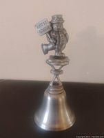 Photo of the solid pewter snowman bell standing upright showing the snowman holding 'LET IT SNOW' sign on the handle and the full bell shape.