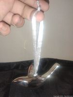 Close-up photo of the silver plated bird ornament held by a hand showing the shiny smooth surface and attached silver ribbon.