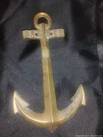 Front view of solid brass anchor decoration on black fabric background.