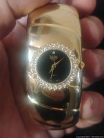 Front view of gold-tone women's cuff watch with black dial and diamond-like stones around face, held in hand.
