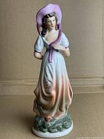 Porcelain figurine of a young woman in a purple bonnet and pastel dress standing on a sculpted green base