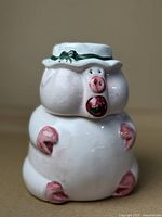 White ceramic pig cookie jar with pink accents and a green hat with bow, front view.