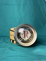 Round crystal paperweight showing design featuring a red 'R' surrounded by a decorative pattern, with box in background.