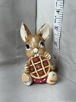 Mouse figurine clutching a red gift with yellow ribbon, measuring approximately 3.5 inches in height via an adjacent ruler.