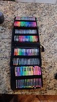 Photo showing an open black zippered case displaying three rows of colored markers in assorted colors arranged in elastic loops.