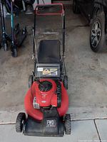 Front view of mower showing red deck, black rear catcher, and handle