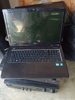 Front view of black Dell laptop showing keyboard, touchpad, screen, and Intel and Windows stickers. Laptop is powered off or screen is inactive.