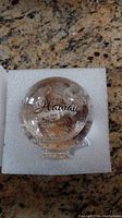 Clear glass globe with seashells inside and 'Hawaii' printed on the front, sitting in white foam padding.