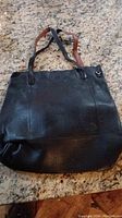 Black leather woman's purse shown from front with two shoulder straps.
