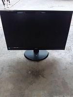 Full front view of the black AOC computer monitor on a concrete floor, showing the entire screen and circular base stand.