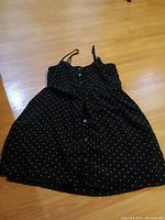Black Volcom women's summer dress laid flat on floor showing front with white polka dot print and buttons.