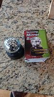 Spinning mirror ball sitting on a countertop next to its original packaging box showing front label with product information.
