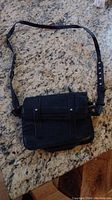 Black leather purse front view on countertop showing flap with strap detail and button accents.