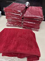 Stack of 12 red bath towels sealed in plastic and one towel unfolded showing the embossed Melrose Country Club crest and text.