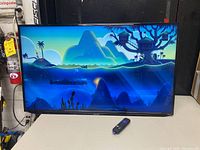 Front view of the Sharp 42-inch flat screen TV powered on showing colorful virtual scene, remote control placed in front.