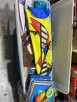 Photo showing bin with various colorful kites and kite books stacked inside.