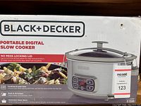 Front of box showing product image, brand, and key features such as cooking on your time, built-in lid hanger, and automatic keep warm.