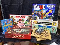 View of entire lot with Clue Giant Edition, Monopoly Nintendo Edition, Monopoly Philadelphia Edition, Scrabble, Hedbanz Junior, chess/checkers board and cards