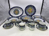 Full view of the set showing dinner plates, teacups with saucers, bowls, and serving platters with colorful geometric and floral patterns and gold trim.