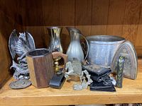 Shelf display of all items, showing pewter dragon, wooden tankard, metal vessels, iron, leather goods, and unicorn figurine.
