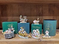 Composite shot of five resin figurines with their original green Walt Disney Gallery boxes on wooden shelf