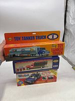 Photo of three boxed collectible toy trucks stacked: a Sunoco toy tanker truck, a 1996 limited edition Mobil truck, and a blue Mobil toy truck.