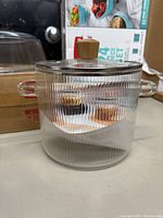 Clear ribbed glass pot with lid featuring wooden knob, two side glass handles visible