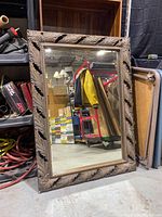 Full view of large rectangular mirror with carved leaf motif frame leaning on floor among other stored items.