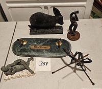 Front view of vintage marble pen holder with 'Bob Hope' plaque, black metal rabbit figurine, bronze reclining female figurine, wooden dancing female figurine, and modern metal bow and arrow figurine.