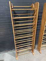 Full view of the oak shoe rack showing its height and structure against a black wall.