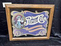 Wide view of framed Pepsi artwork showing full image and frame detail against black cloth background.