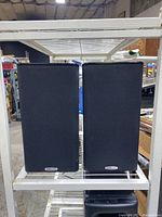 Front view of two Polk Audio bookshelf speakers with black cloth grilles in black wood grain cabinet.