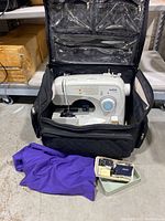 Brother XL-3750 sewing machine inside the black rolling carrying bag with accessories beside it