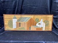Full frontal image of rectangular wooden art panel depicting stylized houses and trees made from painted and natural wood slats in a rustic frame.