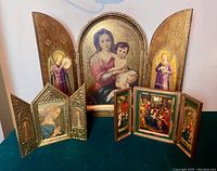 Photo showing all three wooden Florentine triptychs on a green surface, illustrating various sizes and detailed gold gilt religious artwork including Madonna & Child and angels.
