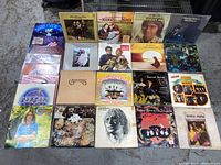 Photo showing front view of 24 various vinyl record albums arranged in grid pattern on floor.